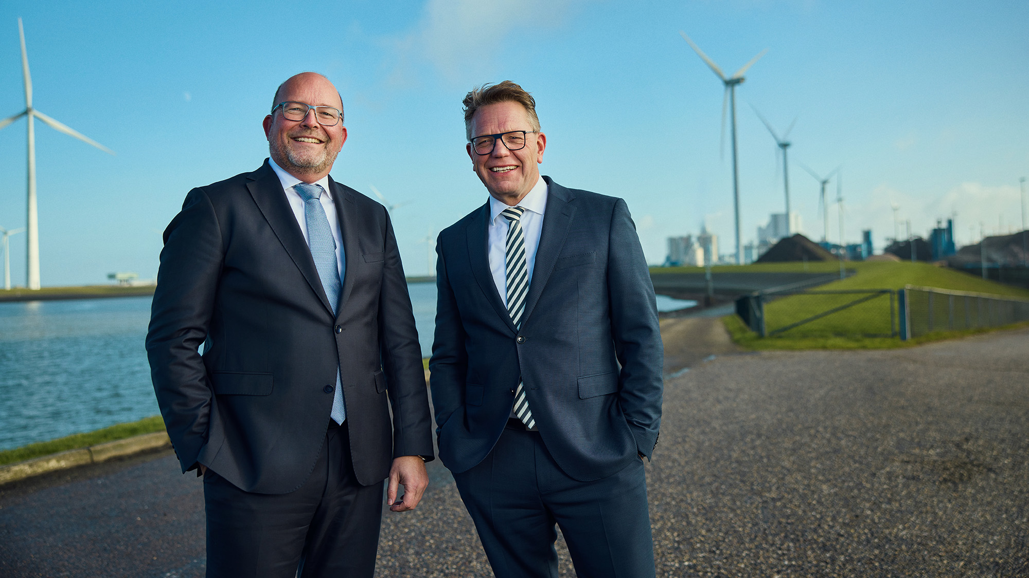 Portretfotografie Groningen – Twee Lachende Mannen In Net Pak Met Windmolens En Eemshaven Op Achtergrond